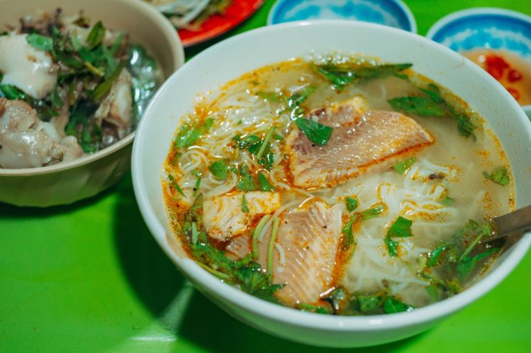 Bowl of bún cá fish noodle soup with fresh herbs and pieces of fish in Nha Trang, Vietnam