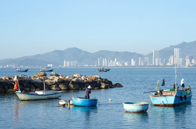 Traditional fishing boats and round basket boats in Nha Trang Bay with the city skyline and mountains in the background
