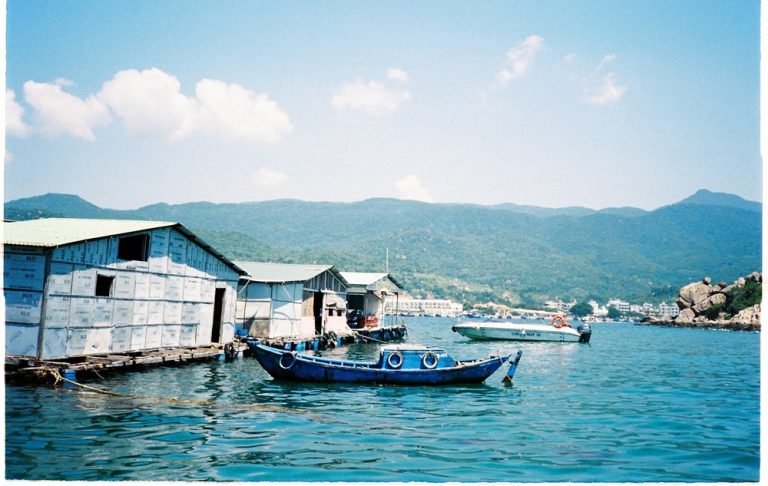 Traditional fishing boat and floating houses on the water near Nha Trang with green mountains in the background Caption Description