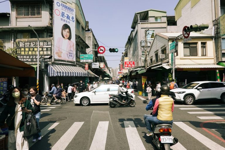 Busy Tainan intersection with scooters, pedestrians, shops and traditional Chinese signs