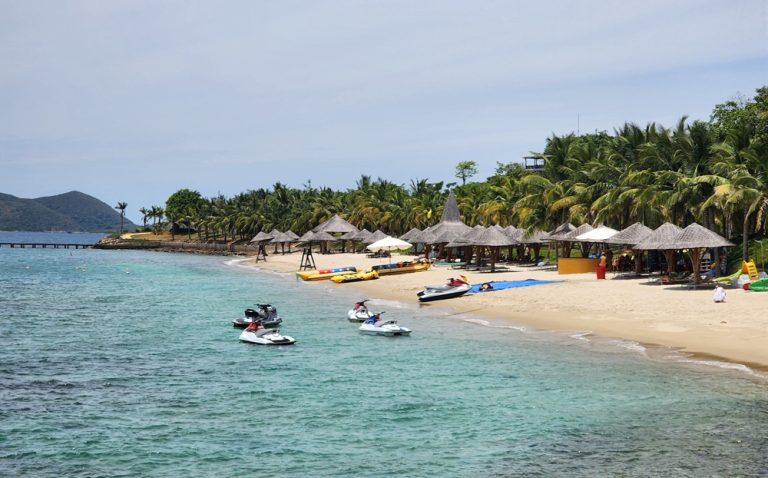 Tropical island beach near Nha Trang with turquoise water, palm trees, beach shelters and jet skis