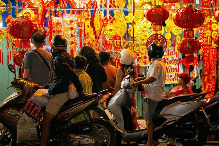 Visitors and scooters beside a colourful market stall filled with red lanterns and decorations at night in Nha Trang
