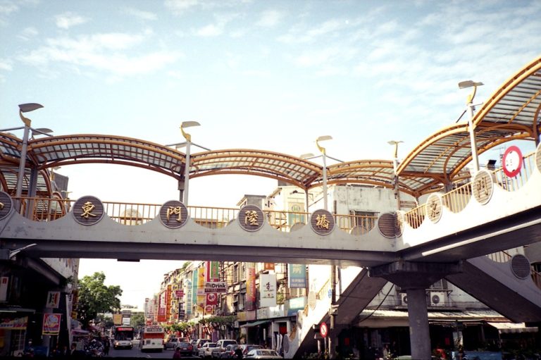 Pedestrian bridge crossing a busy commercial street lined with shops in Tainan