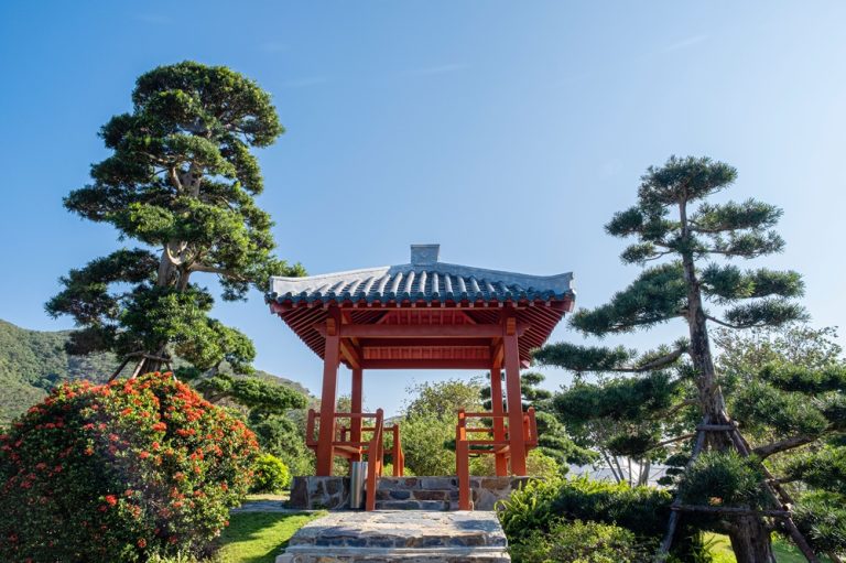 Traditional red pavilion surrounded by landscaped gardens and sculpted trees at Truong Son Craft Village in Nha Trang